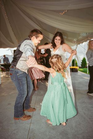 A couple dances under a white draped tent with the person in blue jeans dipping their partner wearing a mint green dress.