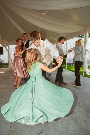 Wedding party dancing under a white tent with guests wearing pastel dresses twirling on the dance floor.