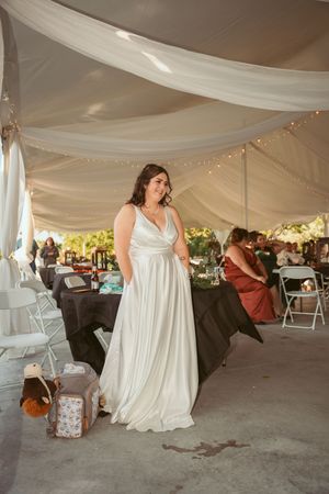 A classic white wedding gown flows elegantly under draped tent fabric with twinkling lights.