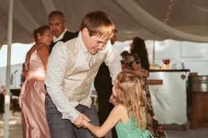 Dancing couples enjoy a lively moment under string lights at an evening wedding reception.