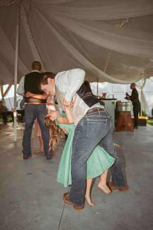 Couples dancing in colorful attire under a draped tent ceiling at an outdoor wedding reception.