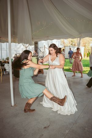 Energetic dancing at a wedding reception under a white tent with someone in cowboy boots.