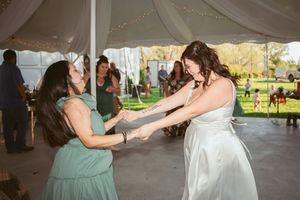 Wedding celebration under a tent with people dancing and white fabric draping overhead.