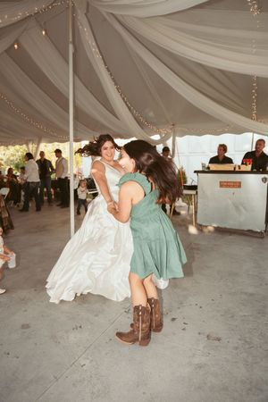 Two people in western boots dance and hug under a tent decorated with white draping and string lights.