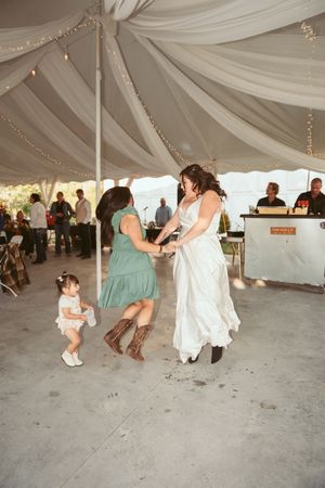 A joyful dance scene under an elegant white tent during a wedding reception with guests dancing on a concrete floor.