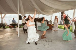 Joyful dancers celebrating on a dance floor under a white tent canopy at an outdoor wedding reception.
