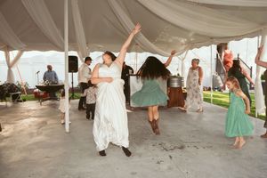 Wedding guests dance together under a white tent during a lively reception celebration.