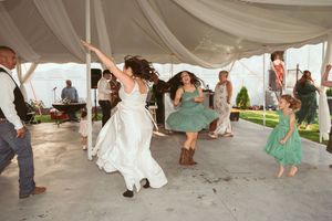 Wedding guests dancing joyfully under a white tent with decorative draping at an outdoor reception.