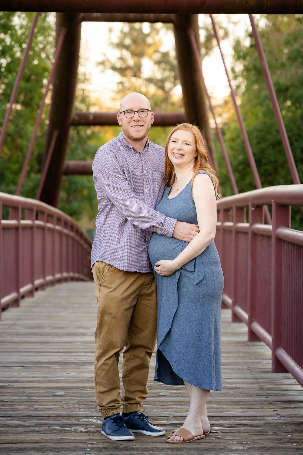 A couple stands on a red bridge for their maternity photo session at golden hour in Bay Area