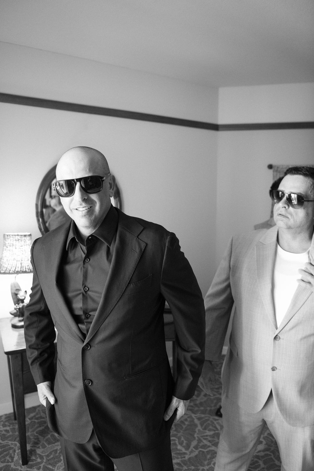 A group of men wearing suits and sunglasses stand together in a monochrome photo reminiscent of a business gathering.