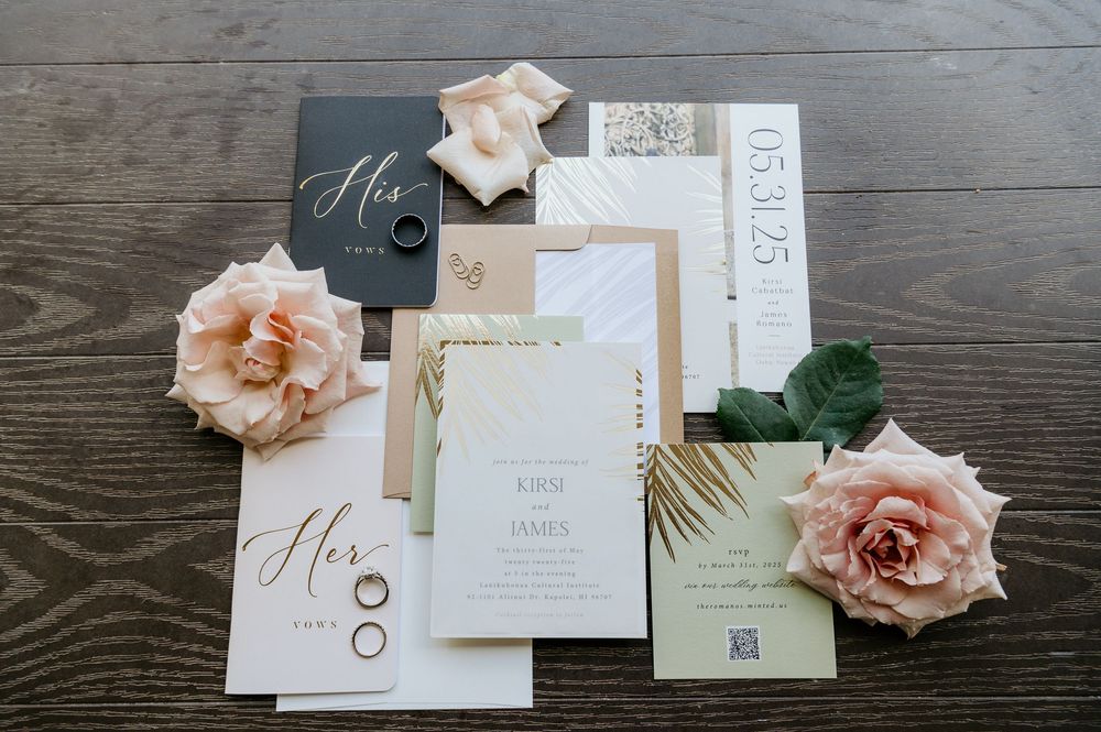 Wedding invitation suite with blush pink roses and elegant calligraphy laid out on a dark wooden surface.