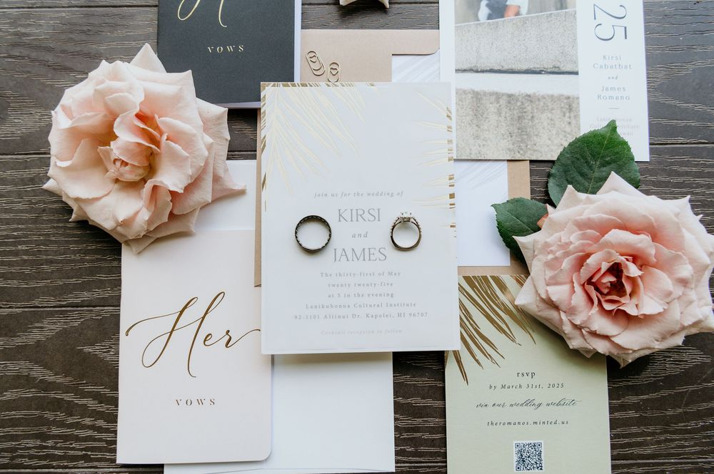 Wedding invitation suite with two silver rings, blush pink roses and elegant calligraphy on wooden background.