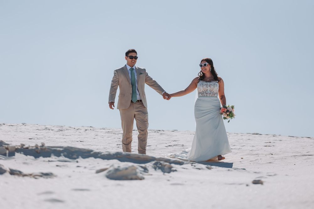 A couple takes romantic portraits on a pristine white sand beach in casual formal wedding attire.