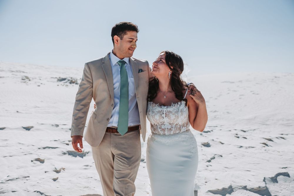 Happy newlyweds walking and laughing together on a scenic white sand beach under cloudy skies.