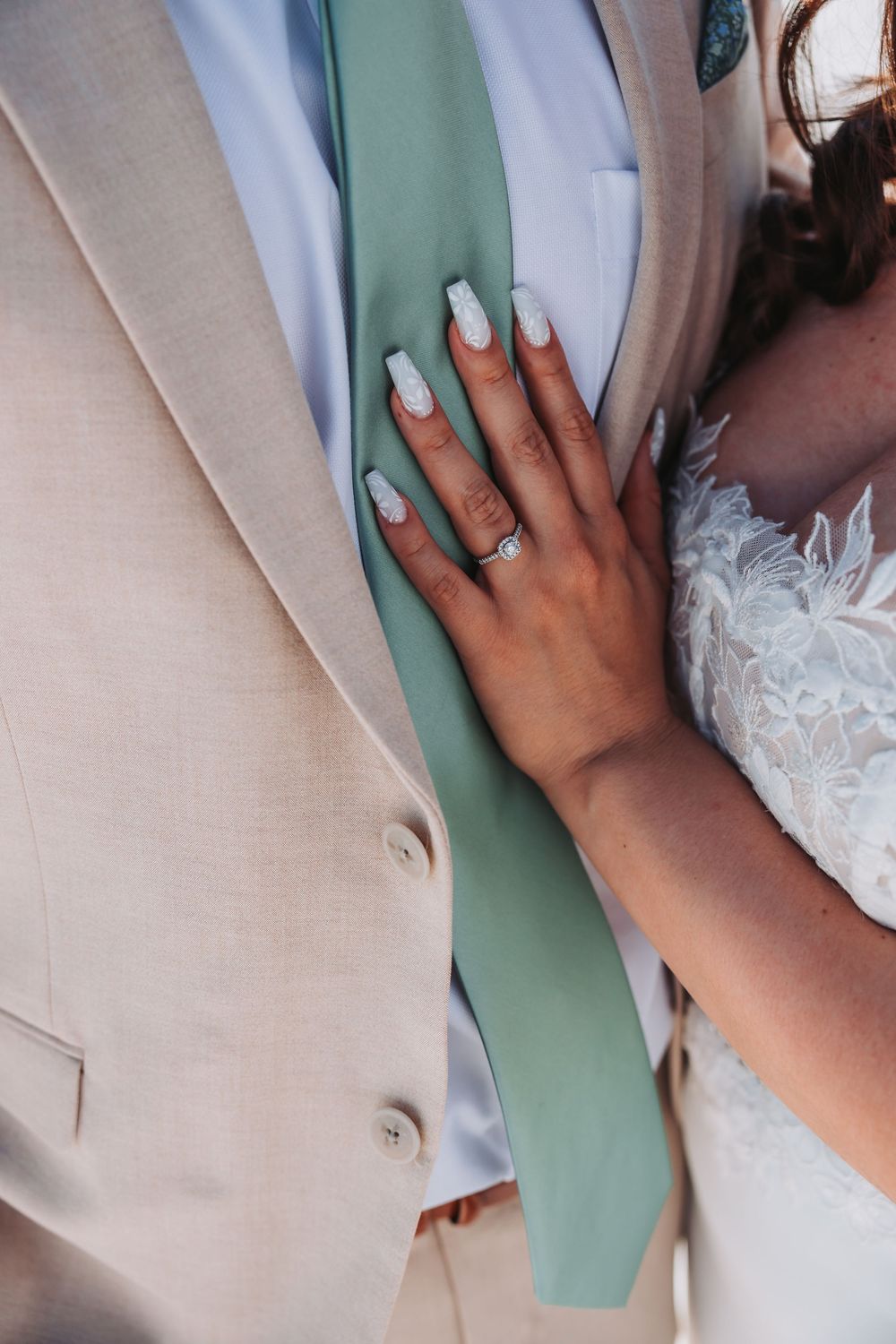 Close up of mint green manicured hand with rings resting on a beige suit jacket and tie.