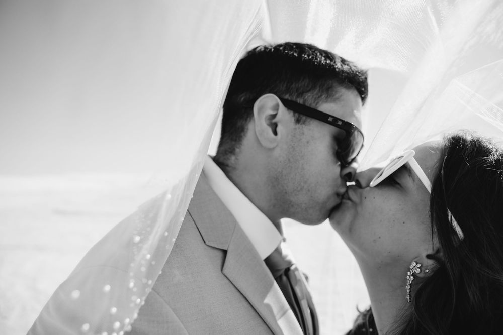 Black and white artistic wedding photo of couple sharing an intimate moment under a veil.