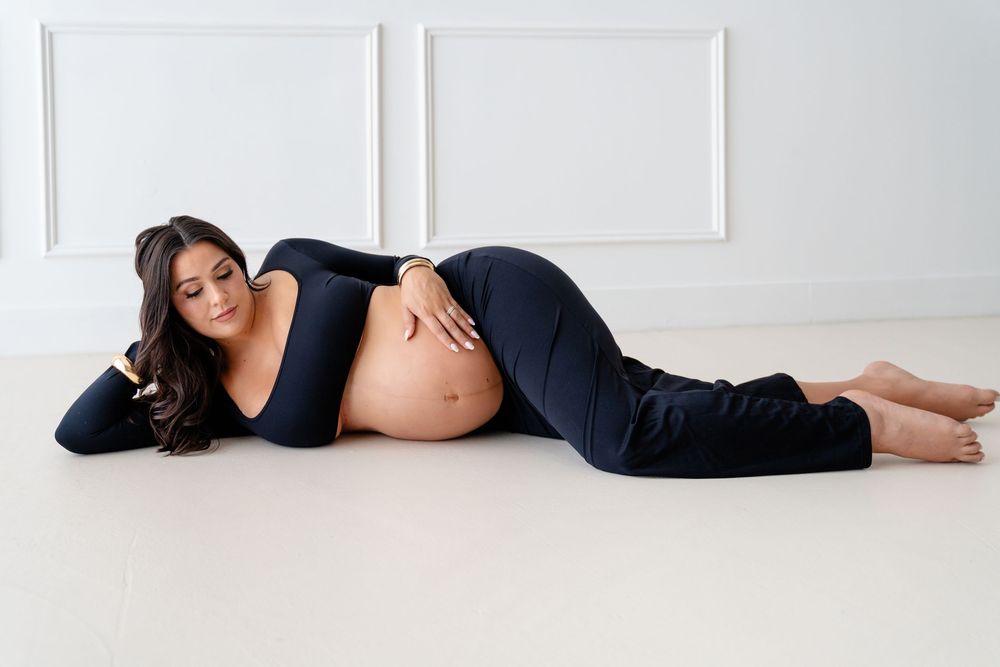 Maternity photo shoot showing pregnant woman in black dress lounging on white floor in connected series of poses.