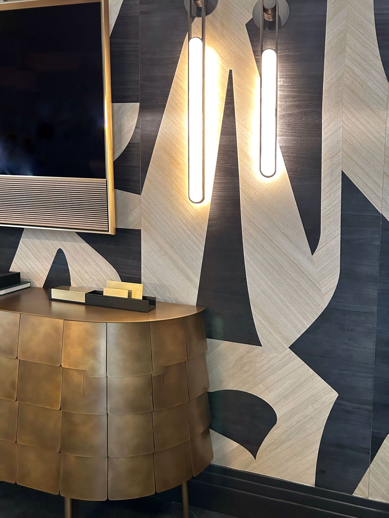Modern wall covering by Phillip Jeffrey with geometric black and white patterns illuminated by elegant pendant lights in a sleek interior.
