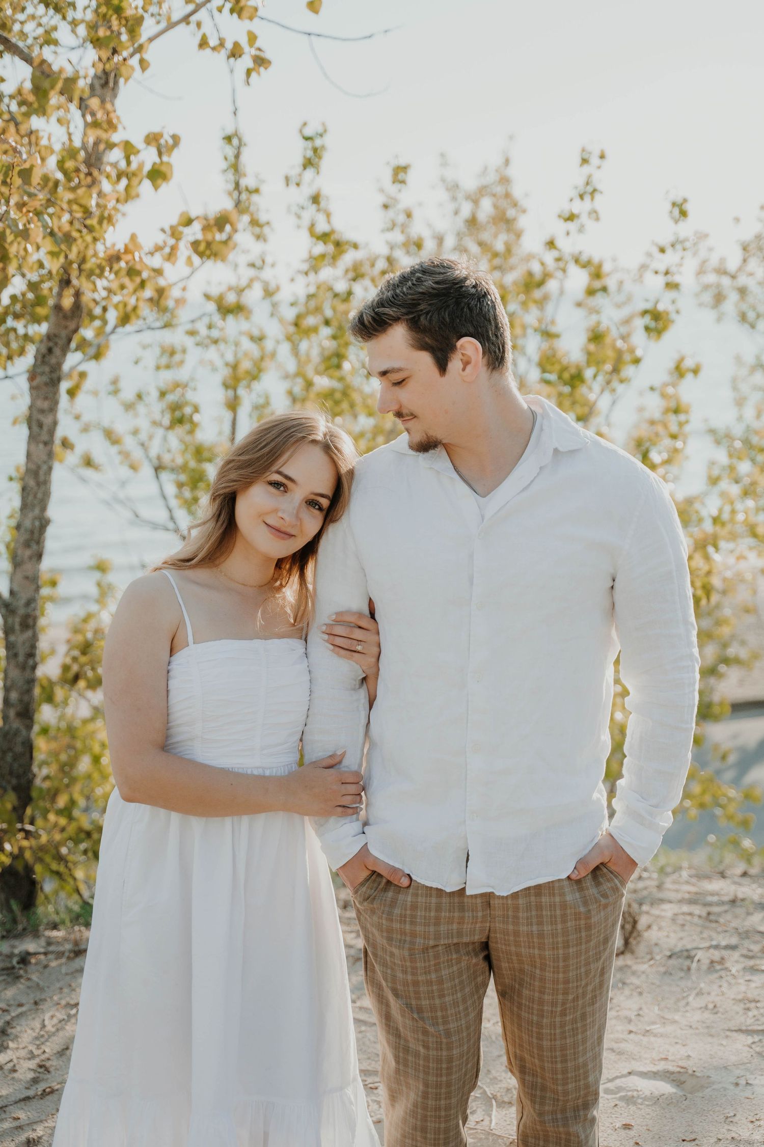 Romantic outdoor couple portrait with autumn leaves in background and warm sunlight creating dreamy atmosphere.