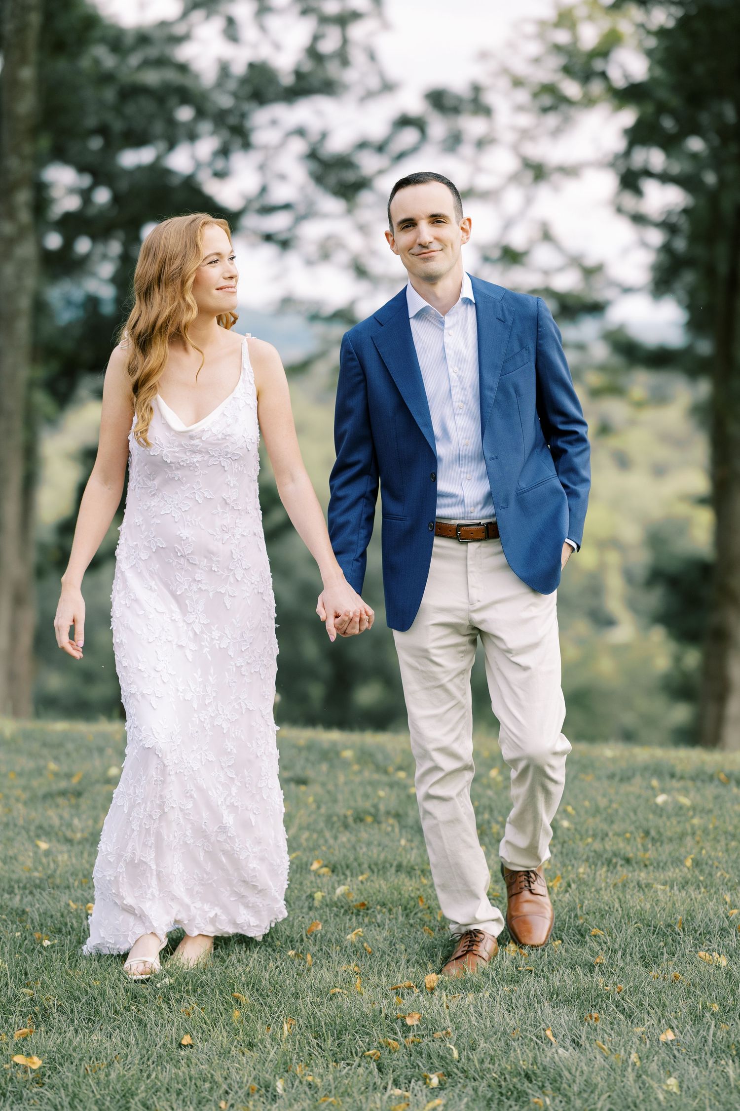 A couple in wedding attire playfully runs through a grassy field on a sunny summer afternoon at Pendry Natirar in Peapack, NJ.