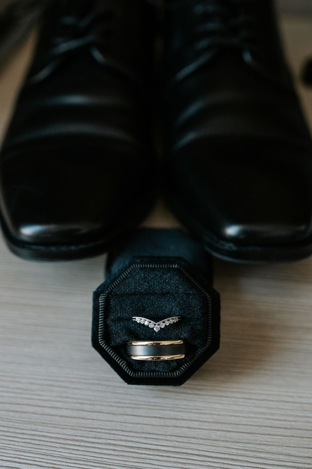 Wedding rings in black octagonal box displayed with formal dress shoes.