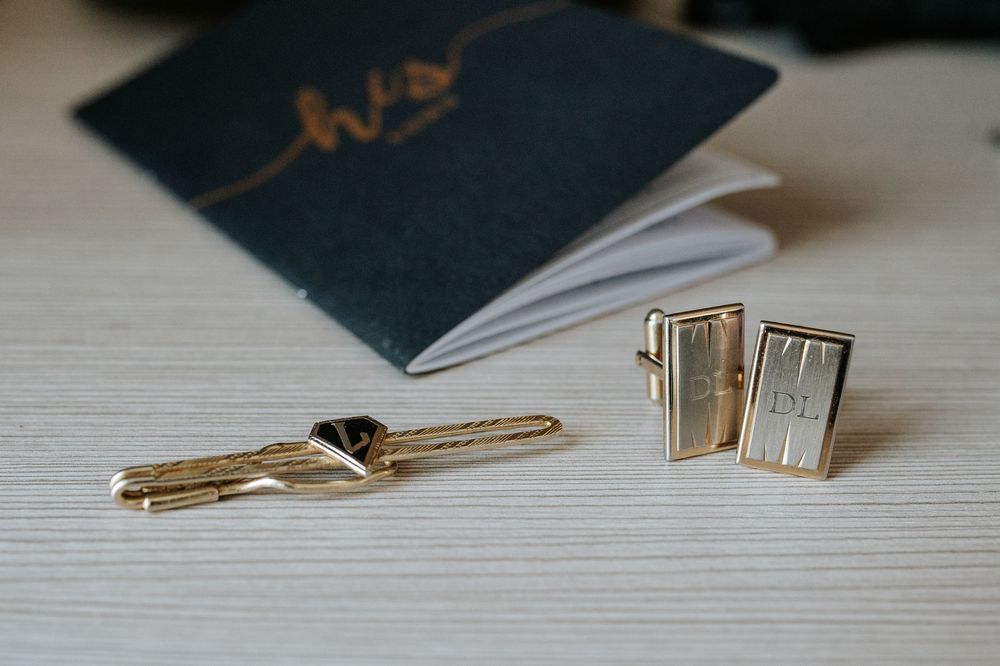 Close-up of black wedding stationery and gold keys arranged on a light wooden surface.