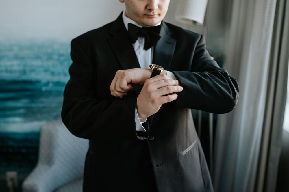 Close-up of groom adjusting watch while wearing black tuxedo.