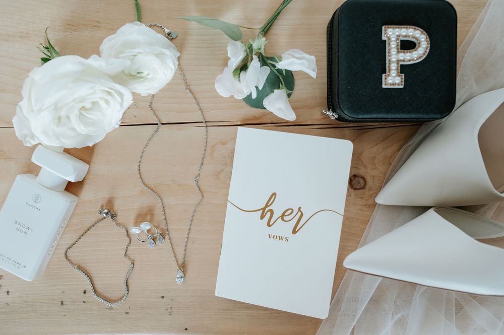 Wedding detail flatlay with white roses, calligraphy and stationery on wooden surface.