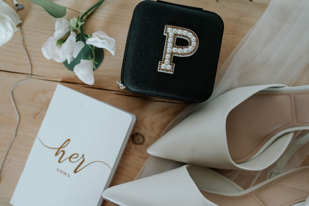 Elegant wedding details with monogram P, vows book, and white bridal shoe.