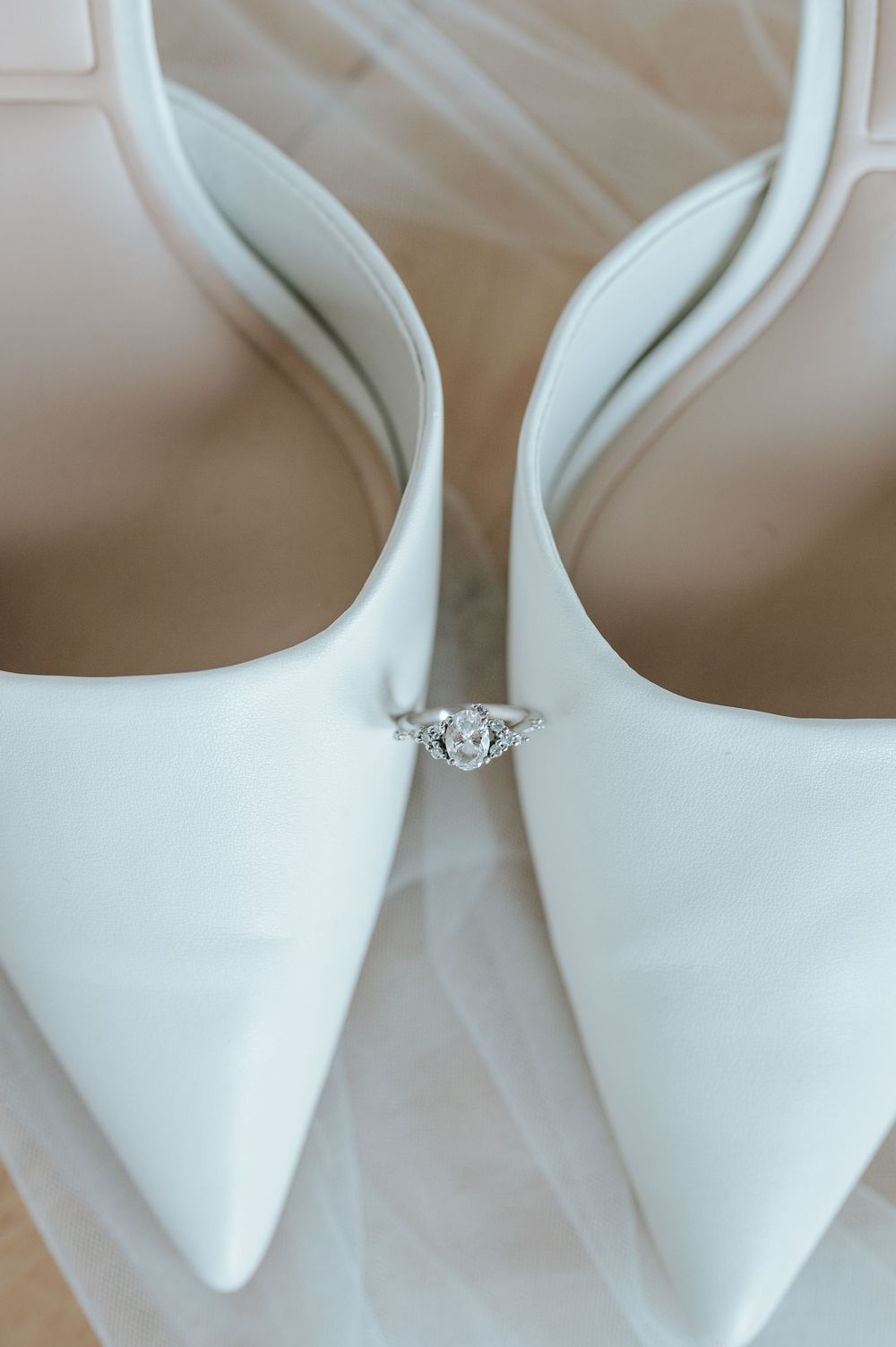 Elegant white bridal shoes with diamond engagement ring detail shot.