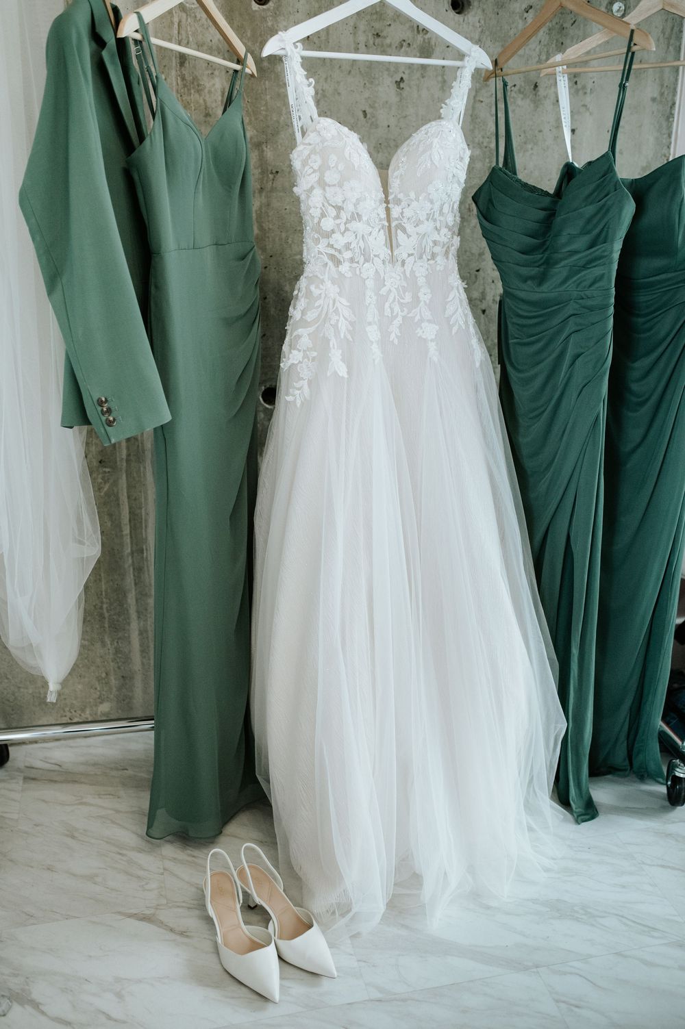 Green bridesmaid dresses and white wedding gown hanging on display.