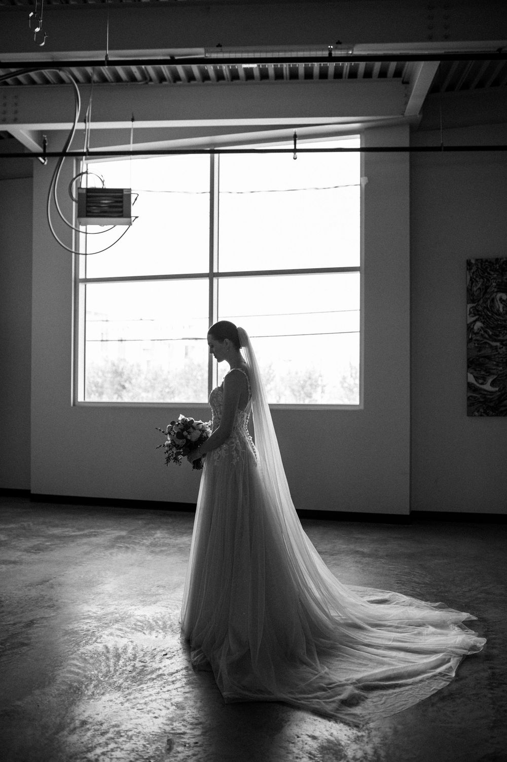 Dramatic black and white silhouette of a wedding dress in an empty room with natural window light.