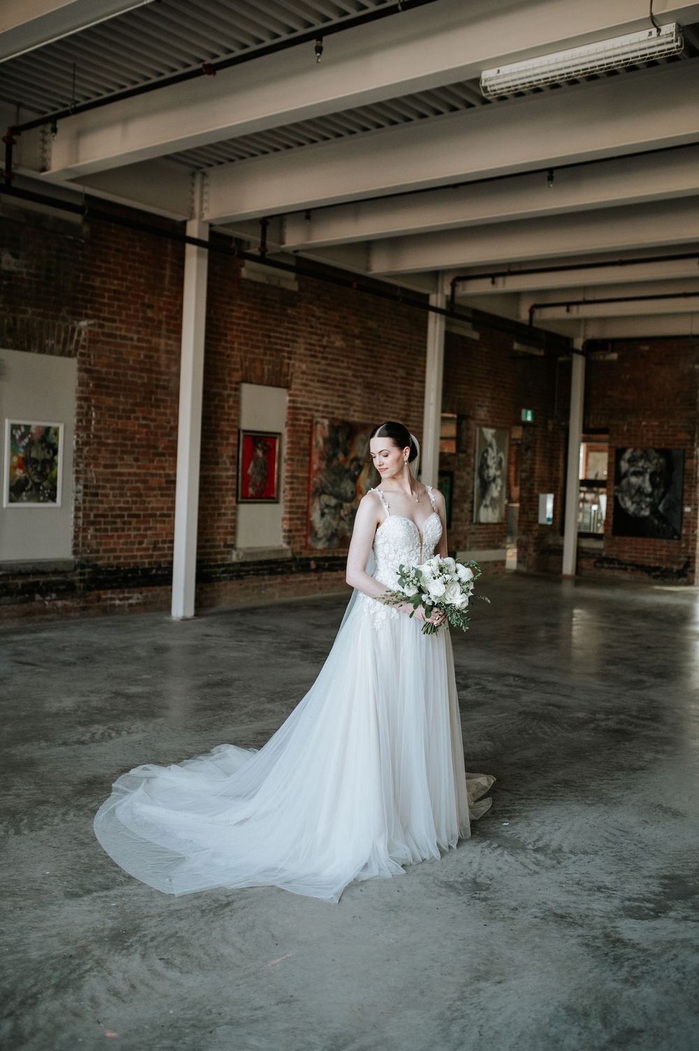 Two white wedding dresses photographed in an industrial brick venue space.