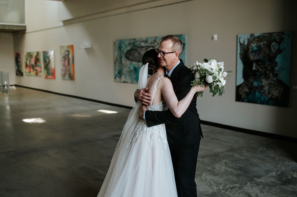 Two people share an emotional embrace during wedding ceremony in an art gallery space.