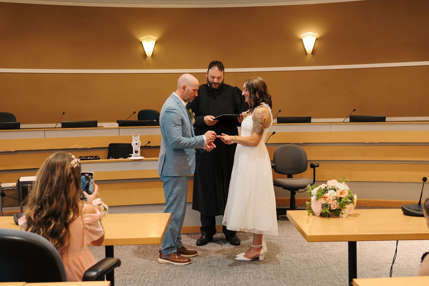 Simple courthouse wedding ceremony in a modern auditorium room with warm lighting and small floral bouquet.