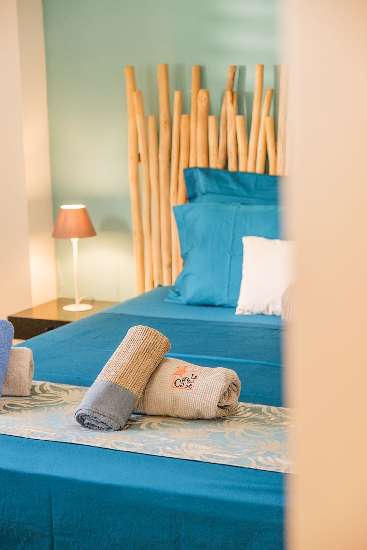 A modern hotel room bed with turquoise blue bedding, bamboo headboard, and white table lamp on nightstand.