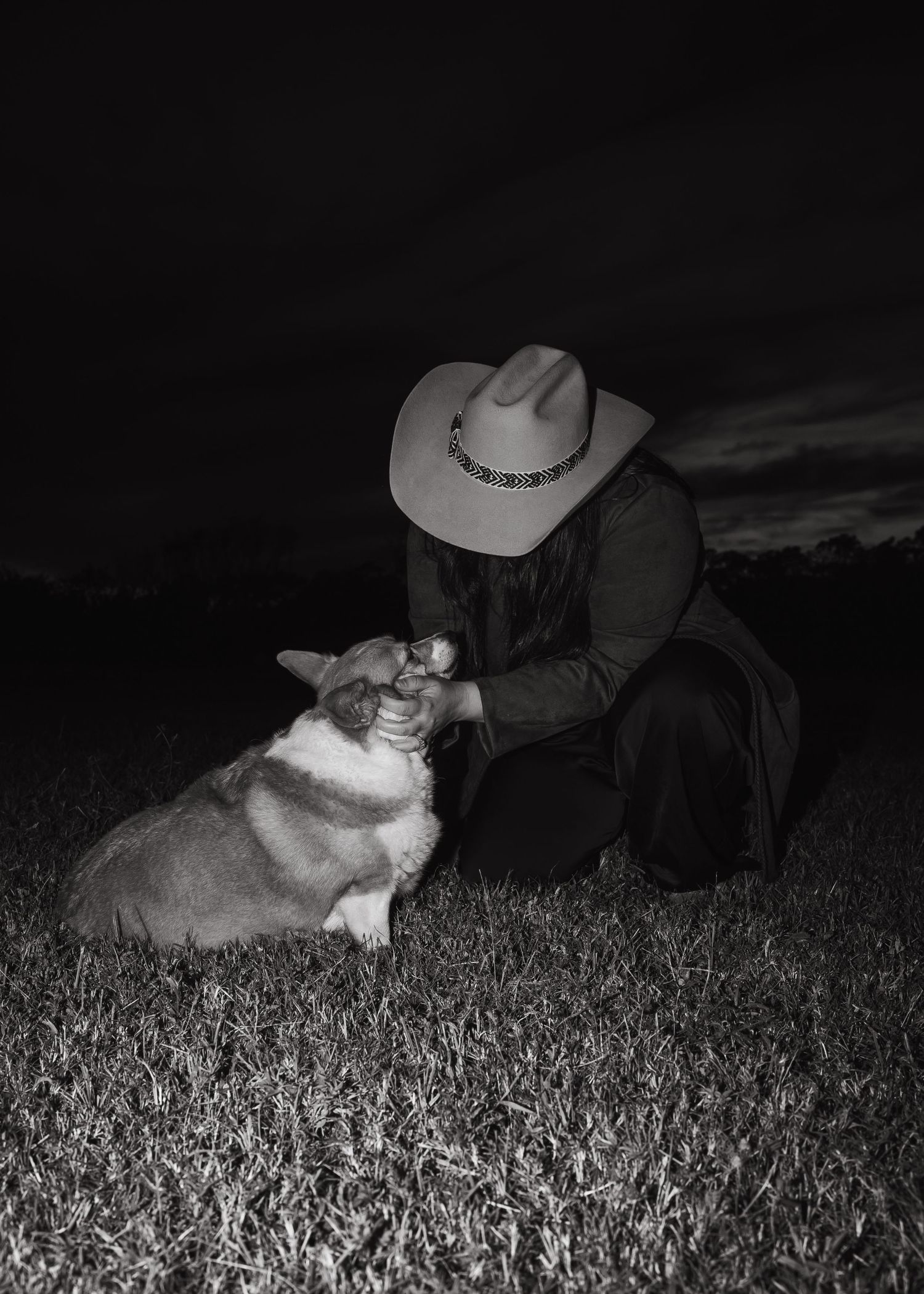 Black and white photograph shows someone lying in a field of wheat or tall grass at night.