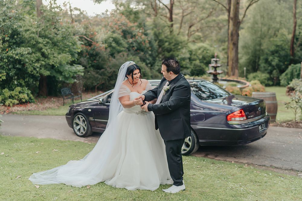 A romantic couple shares an intimate moment during their outdoor wedding ceremony set against a lush green garden backdrop.