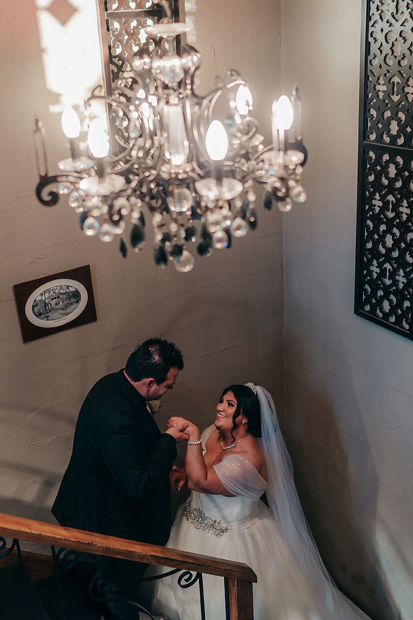 Elegant crystal chandelier illuminates couple in formal attire on staircase during romantic wedding moment.
