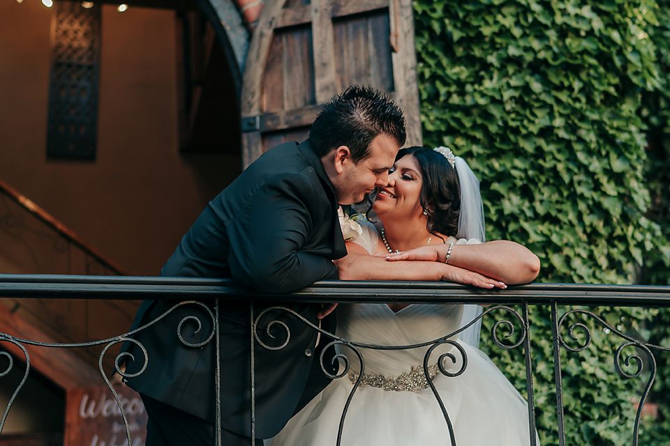 Couples embrace on an ivy-covered balcony at sunset during romantic wedding photoshoot.