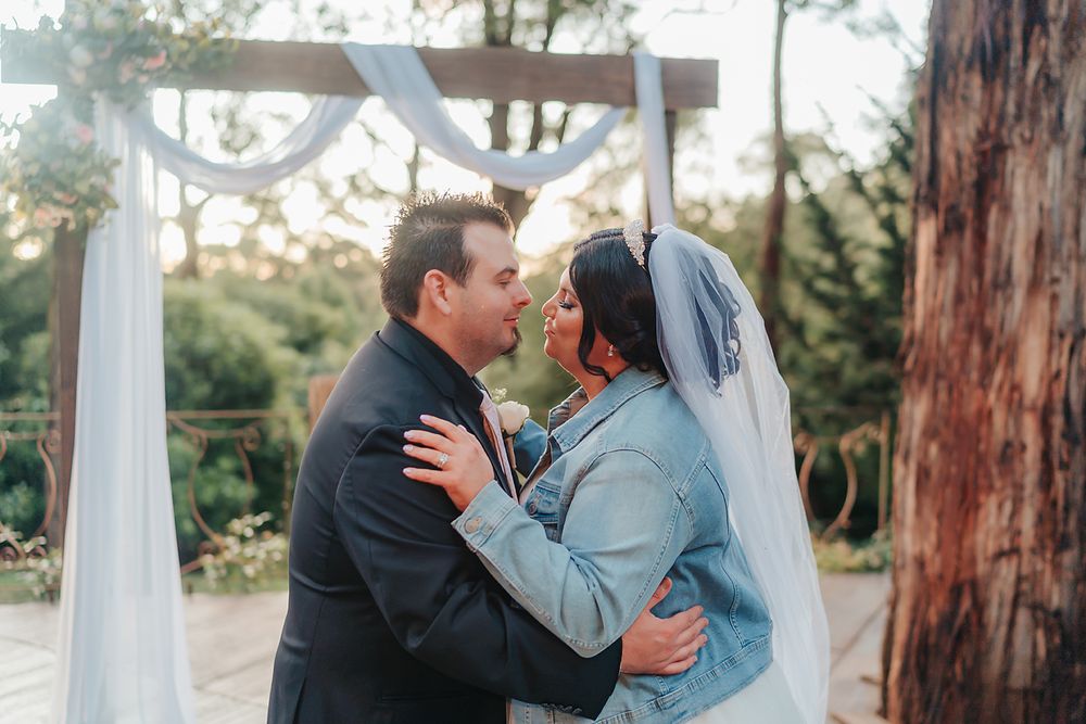 A bride and groom share a romantic moment together among tall trees during their outdoor forest wedding ceremony.