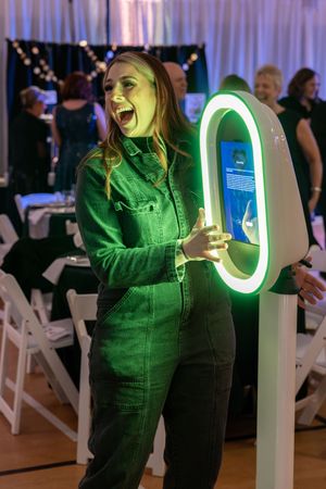 Person in green jumpsuit laughs excitedly while interacting with glowing LED hoop display at indoor event.