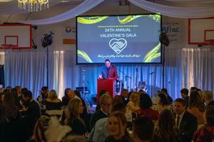 Event attendees gather in a hotel ballroom for a gala with banners and presentation screens visible.