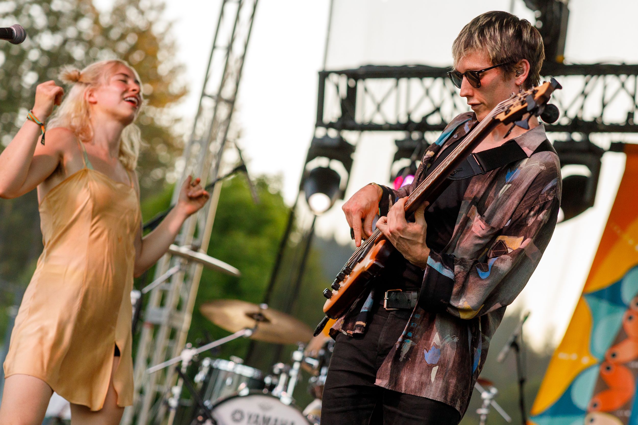 Musicians perform together enthusiastically on an outdoor festival stage with microphones and instruments.