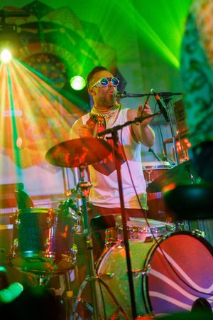 Concert stage illuminated in vibrant green lighting shows musicians performing with instruments in dynamic motion.