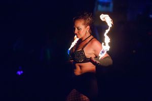 Fire performers creating dramatic displays with flames against dark night sky at an outdoor event.