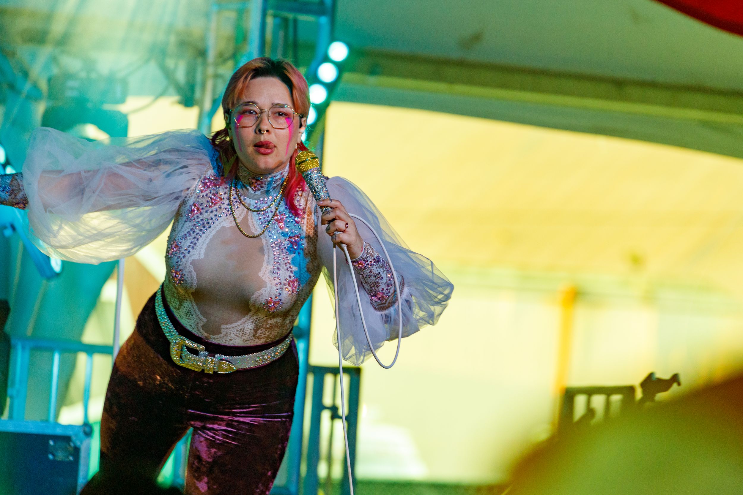 Performer in stylish outfit sings on stage with dramatic yellow lighting effects.