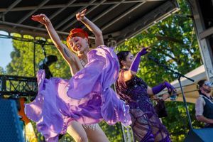 Dancers in flowing purple dresses perform on an outdoor stage during a summer festival.