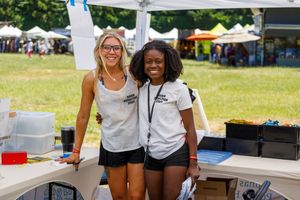 Two volunteers pose together at an outdoor booth during a summer festival event.