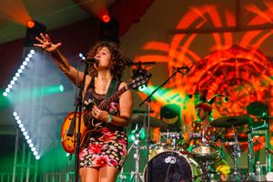 Musician performs passionately on stage with acoustic guitar amid vibrant red and green lighting.